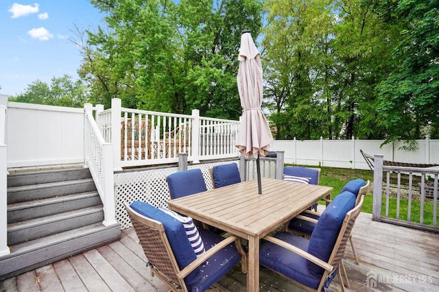 wooden terrace featuring outdoor dining space, a fenced backyard, and stairs