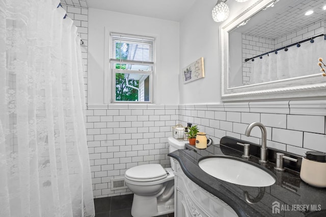 bathroom featuring tile walls, tile patterned floors, toilet, a wainscoted wall, and vanity