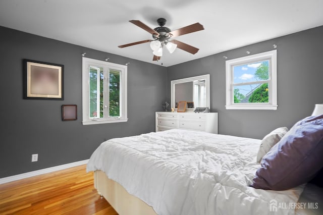 bedroom with multiple windows, light wood-type flooring, baseboards, and a ceiling fan