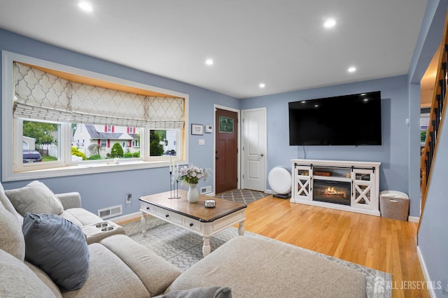 living room featuring baseboards, recessed lighting, wood finished floors, and a glass covered fireplace