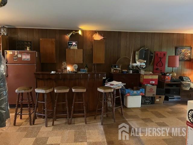 1436 Thomas Ave, North Brunswick, NJ 08902 - kitchen featuring freestanding refrigerator, wood walls, a breakfast bar area, light floors, and dark countertops