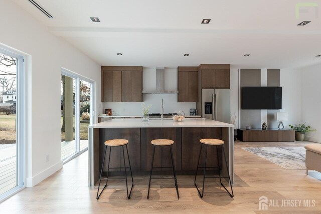 kitchen with wall chimney exhaust hood, stainless steel fridge, light countertops, and modern cabinets