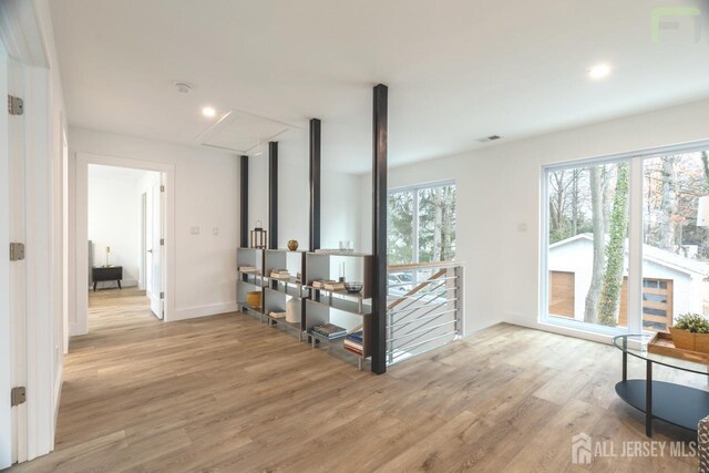 corridor featuring light wood-style flooring, visible vents, a wealth of natural light, and an upstairs landing