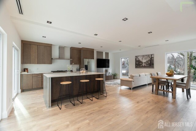 kitchen with a kitchen island with sink, stainless steel appliances, light countertops, wall chimney range hood, and modern cabinets