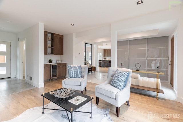 living room featuring light wood-type flooring, wine cooler, visible vents, and plenty of natural light