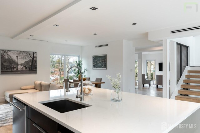 kitchen with dark cabinets, light countertops, a sink, and a center island with sink