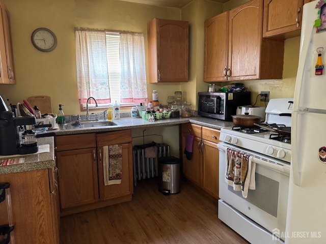 kitchen featuring wood finished floors, white appliances, brown cabinetry, and a sink