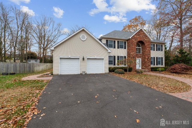 colonial house with an attached garage, fence, aphalt driveway, and brick siding