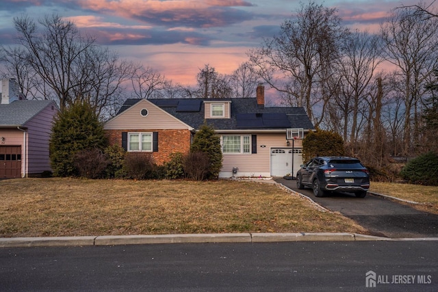 new england style home featuring a lawn, a chimney, aphalt driveway, roof with shingles, and roof mounted solar panels