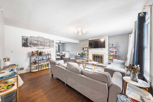 living area with a glass covered fireplace, visible vents, baseboards, and wood finished floors