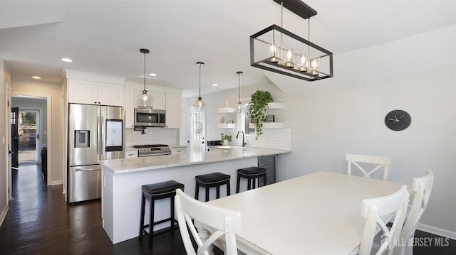 kitchen with a sink, tasteful backsplash, dark wood finished floors, stainless steel appliances, and a peninsula