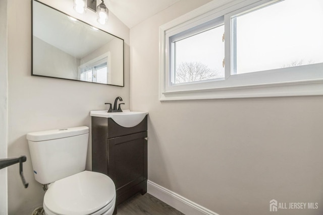 half bathroom featuring baseboards, vanity, toilet, and plenty of natural light