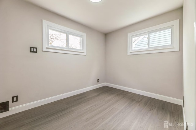 spare room with baseboards, visible vents, plenty of natural light, and wood finished floors