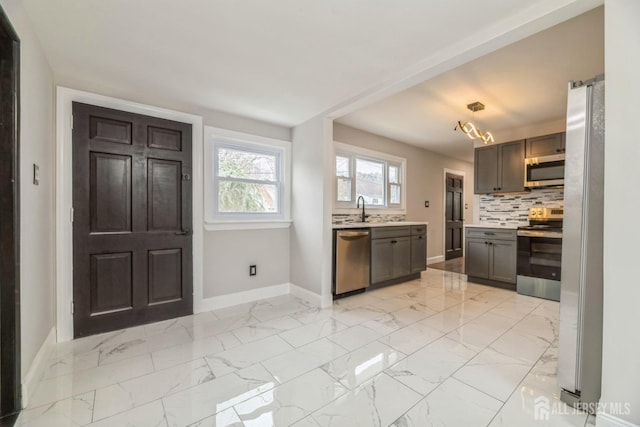 kitchen featuring a sink, stainless steel appliances, backsplash, light countertops, and baseboards