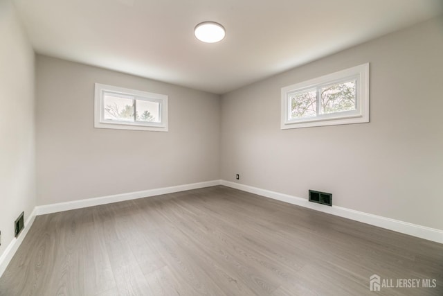 unfurnished room with a wealth of natural light, visible vents, and wood finished floors