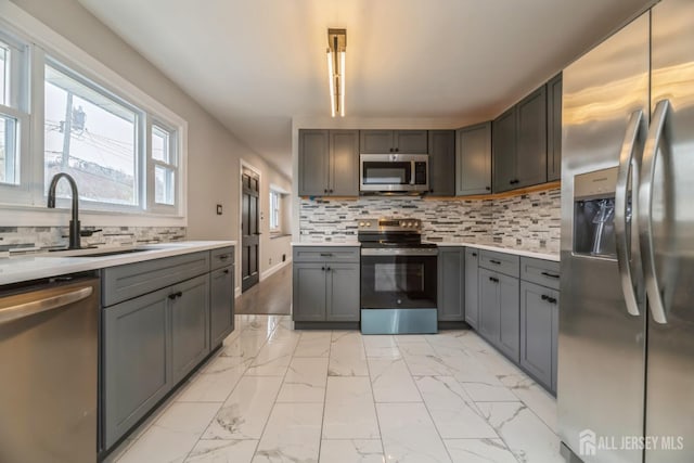 kitchen with stainless steel appliances, marble finish floor, a sink, light countertops, and gray cabinets