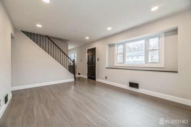 unfurnished living room featuring visible vents, wood finished floors, a healthy amount of sunlight, and stairs
