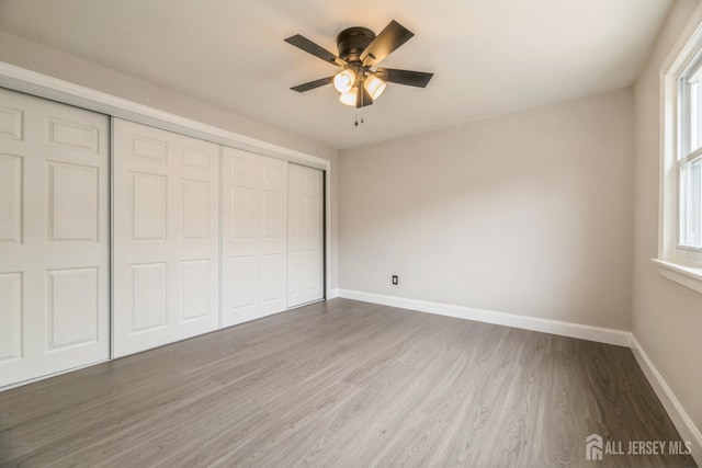 unfurnished bedroom with baseboards, a closet, multiple windows, and wood finished floors