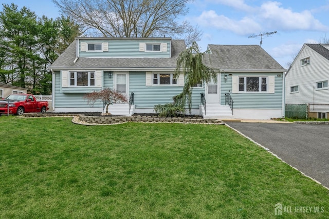 view of front of home with roof with shingles, entry steps, and a front yard