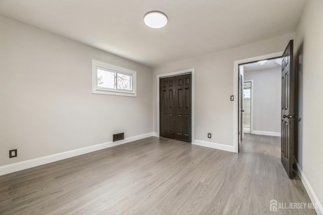 unfurnished bedroom featuring baseboards, a closet, visible vents, and wood finished floors