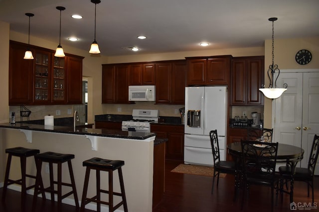 kitchen with dark wood-type flooring, decorative light fixtures, white appliances, and kitchen peninsula