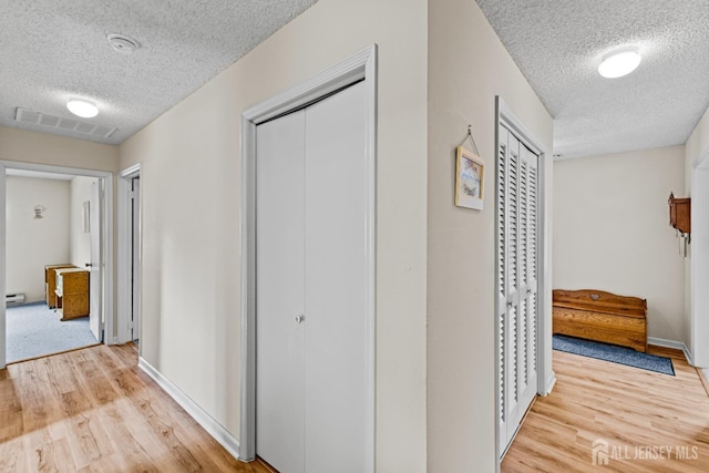 corridor featuring light wood finished floors, visible vents, a textured ceiling, and baseboards