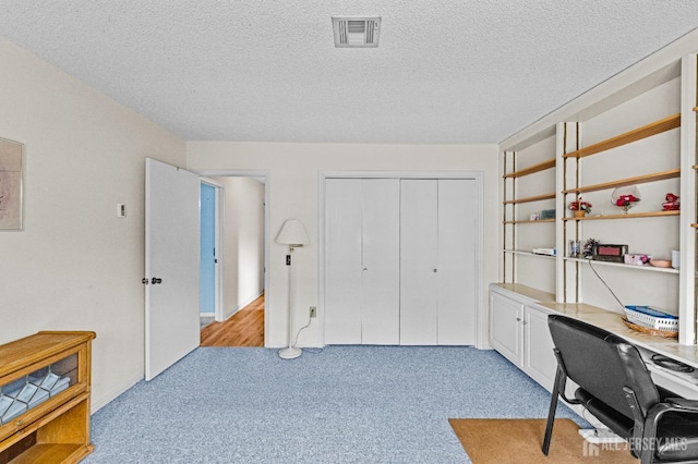 office featuring a textured ceiling, visible vents, and light carpet