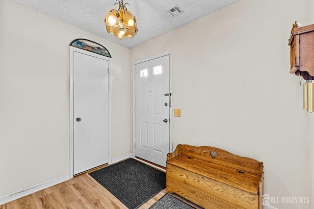 entrance foyer with visible vents, light wood-style flooring, a textured ceiling, and an inviting chandelier