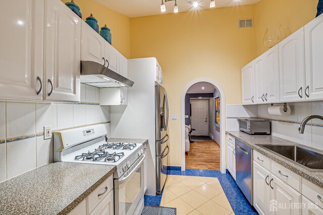 kitchen featuring appliances with stainless steel finishes, sink, range hood, white cabinetry, and light tile patterned flooring