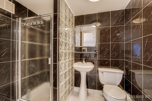 bathroom with tile patterned floors, a shower with shower door, tile walls, and toilet