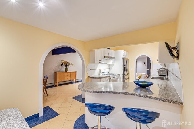 kitchen with stainless steel fridge, white gas range oven, baseboard heating, sink, and white cabinetry