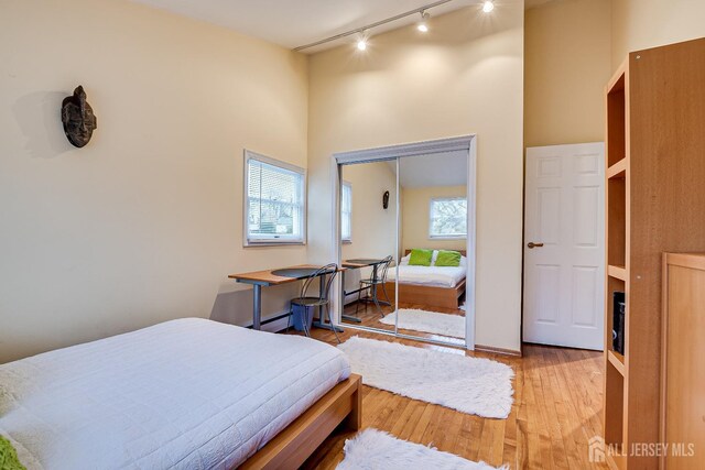 bedroom with track lighting, light hardwood / wood-style flooring, and a closet