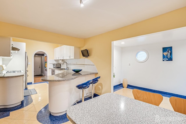 kitchen featuring kitchen peninsula, decorative backsplash, sink, light tile patterned floors, and white cabinetry