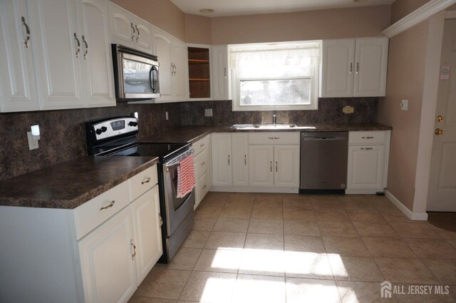 kitchen featuring light tile patterned floors, dark countertops, appliances with stainless steel finishes, white cabinetry, and a sink