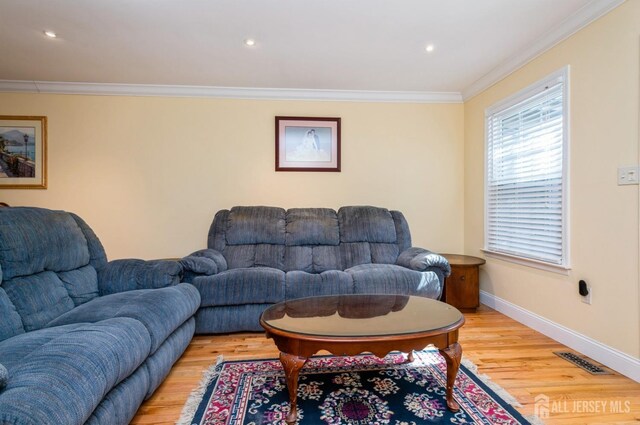 living room featuring baseboards, visible vents, ornamental molding, and light wood-type flooring