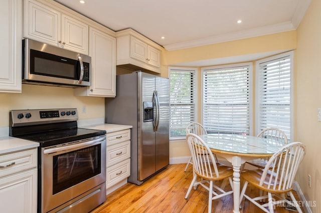 kitchen with ornamental molding, light countertops, cream cabinetry, light wood finished floors, and appliances with stainless steel finishes