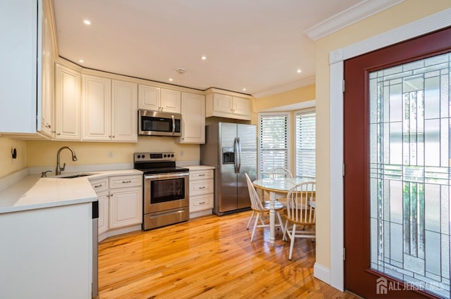 kitchen featuring crown molding, appliances with stainless steel finishes, a sink, light countertops, and light wood-type flooring