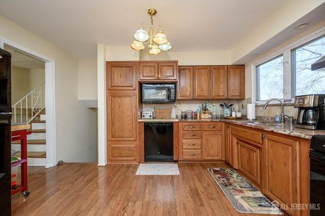 kitchen with light hardwood / wood-style floors, black appliances, light stone countertops, pendant lighting, and sink