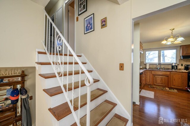 staircase with a notable chandelier, sink, and hardwood / wood-style flooring