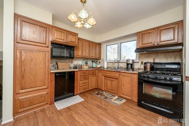 kitchen with pendant lighting, black appliances, decorative backsplash, sink, and light wood-type flooring