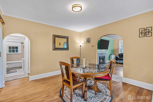 425 Grove Ave, Metuchen, NJ 08840 - dining space with arched walkways, light wood-style floors, crown molding, and a lit fireplace