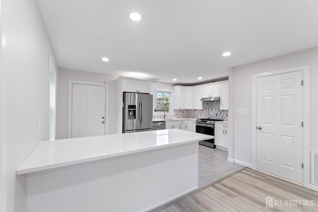763 Gadek Pl, Perth Amboy, NJ 08861 - kitchen featuring appliances with stainless steel finishes, white cabinets, light wood-style floors, a peninsula, and under cabinet range hood