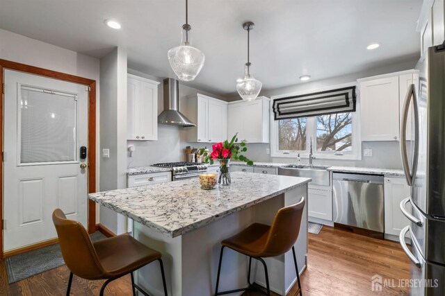 kitchen featuring sink, white cabinetry, wall chimney range hood, pendant lighting, and appliances with stainless steel finishes