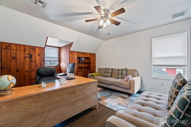 office featuring dark wood-type flooring, vaulted ceiling, wood walls, built in shelves, and ceiling fan