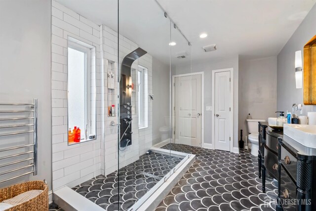 bathroom with toilet, a tile shower, radiator heating unit, a healthy amount of sunlight, and vanity