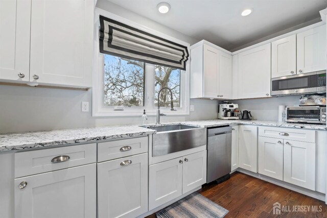 kitchen with light stone counters, dark wood-type flooring, stainless steel appliances, white cabinetry, and sink