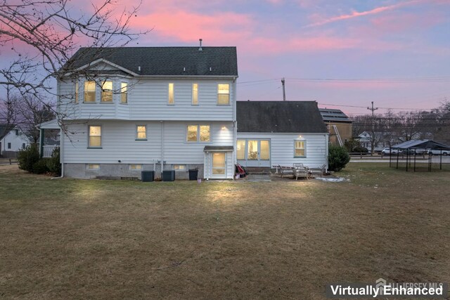 back house at dusk with a yard, central AC unit, and a trampoline