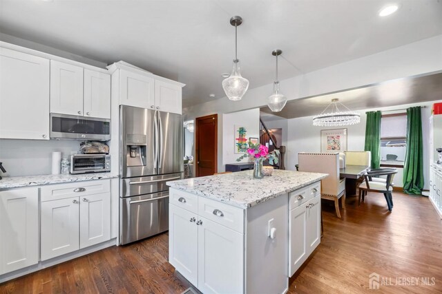 kitchen featuring appliances with stainless steel finishes, light stone countertops, pendant lighting, dark wood-type flooring, and white cabinetry