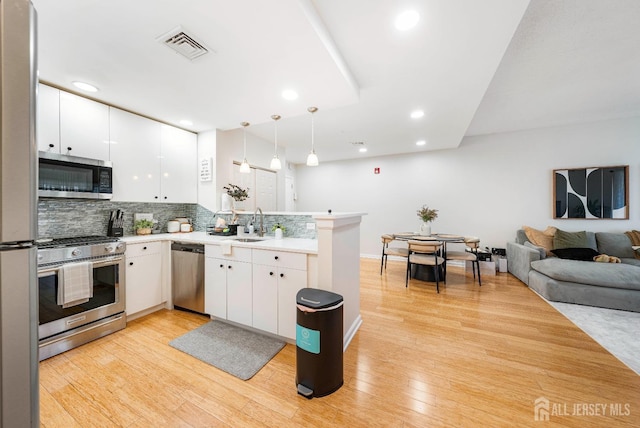 kitchen with stainless steel appliances, a peninsula, white cabinets, decorative backsplash, and light countertops