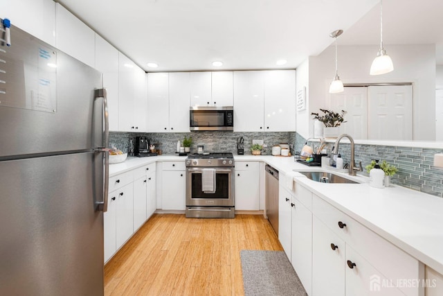 kitchen with appliances with stainless steel finishes, a sink, tasteful backsplash, white cabinetry, and light wood finished floors